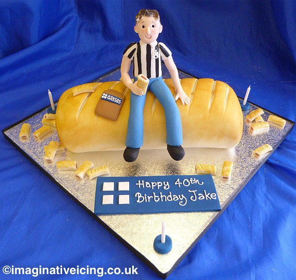 Greggs Sausage Roll shaped Birthday Cake with icing model of the birthday person eating a sausage roll.